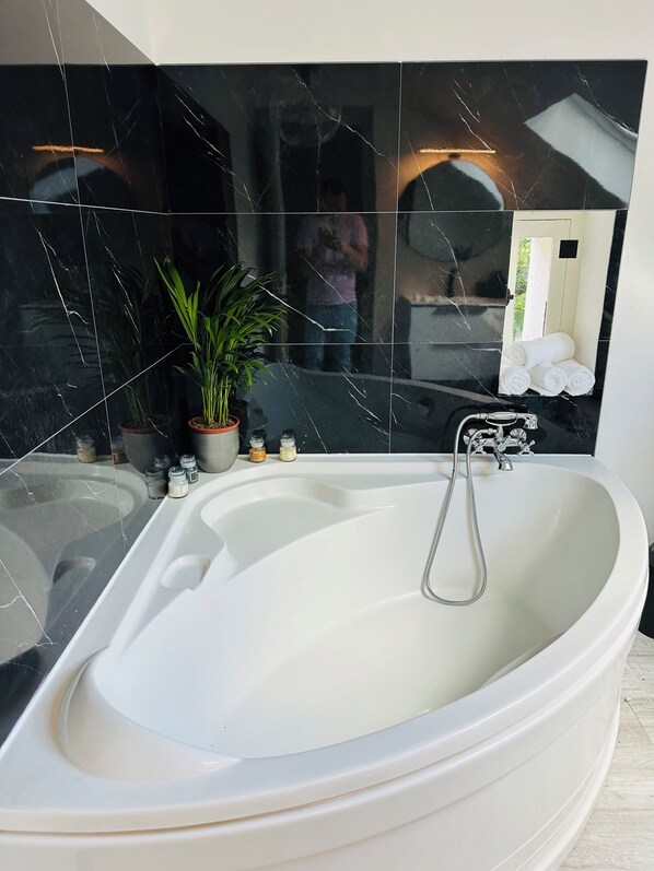 A modern bathroom with a freestanding bathtub, a potted plant, and toiletries on the counter.