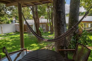 A hammock between trees, a wooden table, and a chair in a garden area. - Charm Suites Masters (Arraial d' Ajuda)