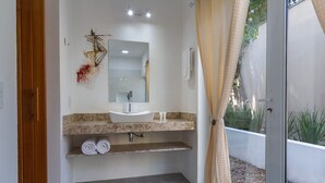 Ein modernes Badezimmer mit Waschbecken in Weiß, einem großen Spiegel und einer sichtbaren Duschkabine durch eine Glastür.