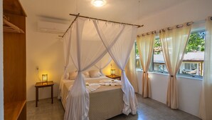 Ein Schlafzimmer mit einem Himmelbett, einem Nachttisch mit Lampe und einem Fenster mit Vorhängen.