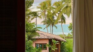 Blick aus einem Fenster auf einen Strand, Palmen und ein kleines Gebäude mit einem Ziegeldach.