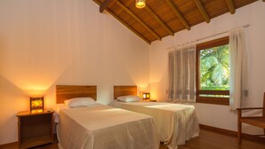 A bedroom with two beds, wooden headboards, bedside lamps, a wooden chair, and a window with curtains. - Apartament "Premium Comfort", perfect for families (Arraial D'Ajuda)