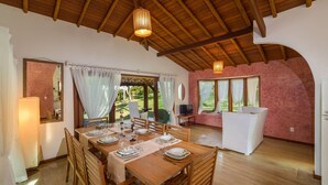 A dining area with a wooden table set for four, surrounded by wooden chairs. There is a large window with curtains, a mirror on the wall, and a ceiling with exposed beams. - Individual "Lux" villa with private pool (Arraial D'Ajuda)