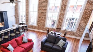 A spacious living area with a red and black sofa set, a dining table with chairs, and large windows with a view of the city. - Jellyfish Lookout on Strand- historic neighborhood, local shops and dining (Galveston)