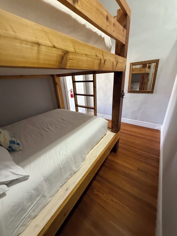 Un lit superposé dans une pièce dont le sol est en bois et les murs sont blancs.