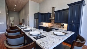 A modern kitchen with dark blue cabinets, a granite countertop, and a long dining table set for six. - Jellyfish Lookout on Strand- historic neighborhood, local shops and dining (Galveston)