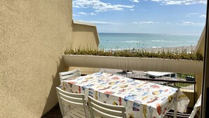 A balcony with a table and chairs, overlooking a beach with a clear sky. -  SE085 - new two-room apartment facing the sea at the ''Pyramids'' (Senigallia)