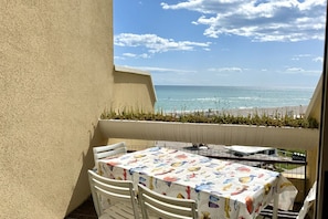 A balcony with a table and chairs, overlooking a beach with a clear sky. -  SE085 - new two-room apartment facing the sea at the ''Pyramids'' (Senigallia)