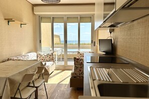 Een moderne keuken met een eethoek, een televisie en uitzicht op zee door grote schuifdeuren.