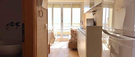 A modern kitchen with a refrigerator, a telephone, and a window with a view of a balcony.
