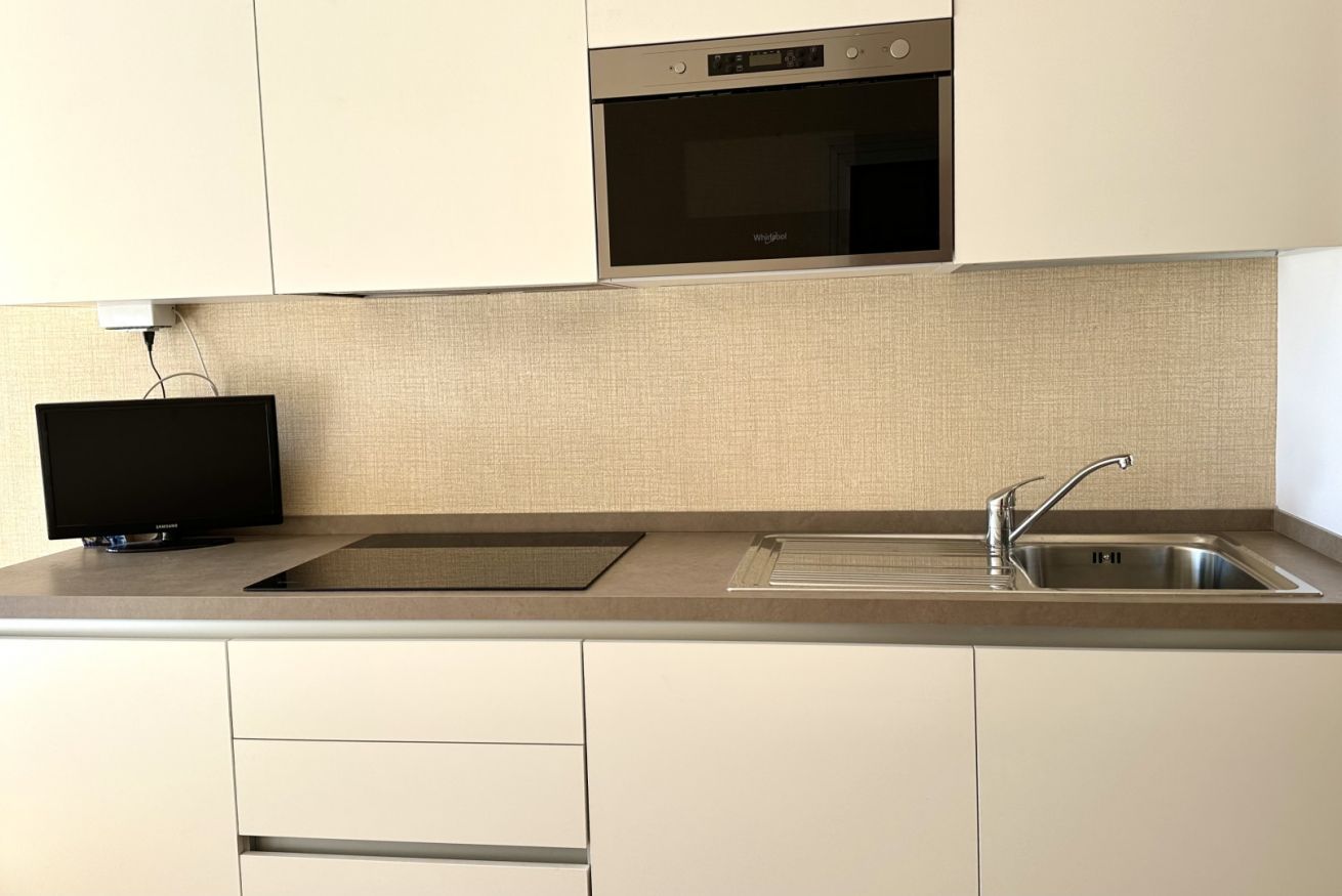 A modern kitchen with a built-in oven, a flat-screen TV, and a stainless steel sink.