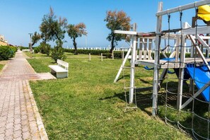 Un parco con un viale lastricato, una panchina in legno e un'area giochi.