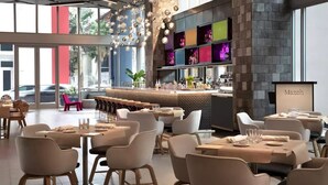 A modern restaurant interior with multiple dining tables and chairs, a bar area, and a large window offering a view of the street. - Apartment Downtown Miami (Miami)