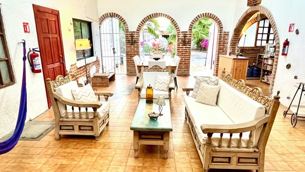 A spacious living area with a sofa set, a coffee table, and a dining table. There are arched doorways leading to outdoor areas. - Room #3 two blocks from the Malecon (La Paz)