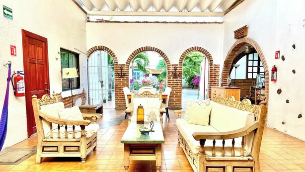 A cozy lounge area with two wooden sofas, a coffee table, and a brick wall with arched windows. - Room #2 two blocks from the Malecon (La Paz)