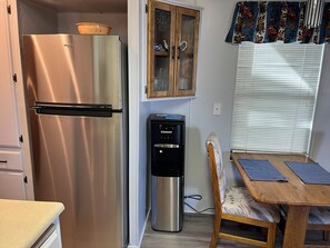 A kitchenette with a stainless steel refrigerator, a water dispenser, and a wooden dining table with chairs. - Voyager RV Resort & Hotel Vacation Rental Walk to the beautiful Sonoran Desert! (Tucson)