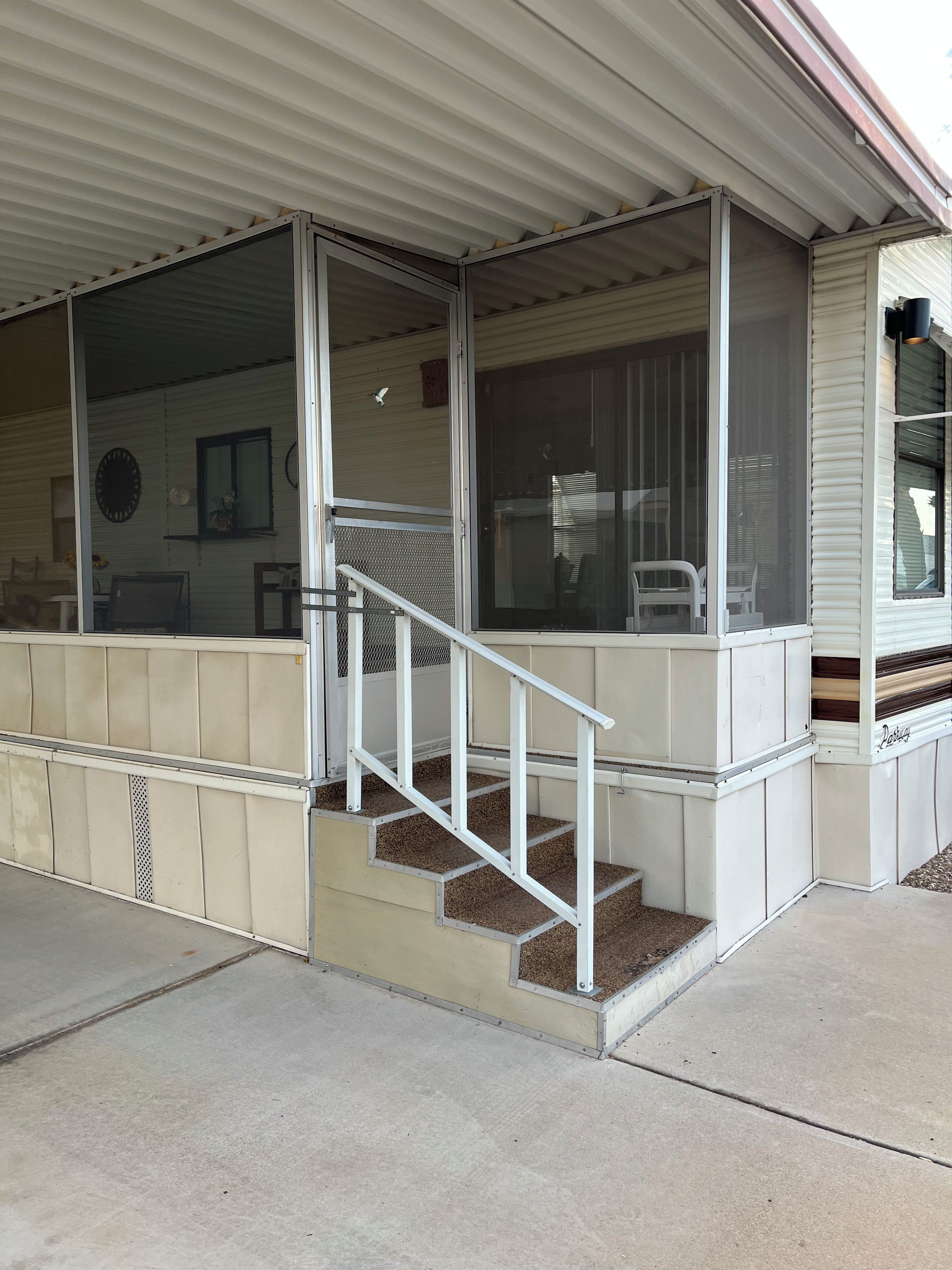 A covered porch with a set of stairs leading to a door, a window, and a chair outside.
