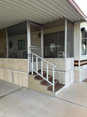 A covered porch with a set of stairs leading to a door, a window, and a chair outside. - Voyager RV Resort & Hotel Vacation Rental Walk to the beautiful Sonoran Desert! (Tucson)