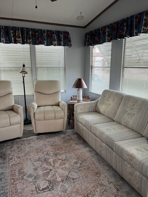 A living room with a beige sofa, two armchairs, a floor lamp, and a patterned rug.
