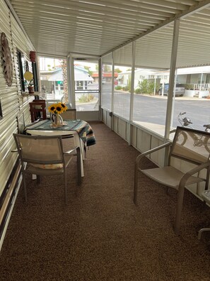 A covered patio area with a table and chairs, a window with a view of the street, and a door leading outside. - Voyager RV Resort & Hotel Vacation Rental Walk to the beautiful Sonoran Desert! (Tucson)