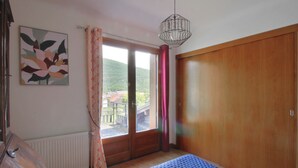 Une chambre à coucher comprenant un lit, une armoire en bois, un radiateur, une fenêtre avec des rideaux et un luminaire suspendu.