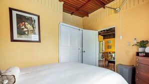 A bedroom with a bed, a wardrobe, a dresser, a framed picture, and a door leading to another room.