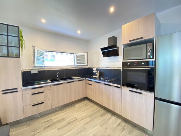 A modern kitchen with light wood cabinets, a black countertop, stainless steel appliances, and a window providing natural light.