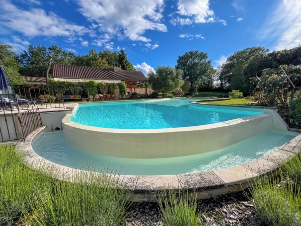A swimming pool with a curved edge, surrounded by a stone deck and grass.