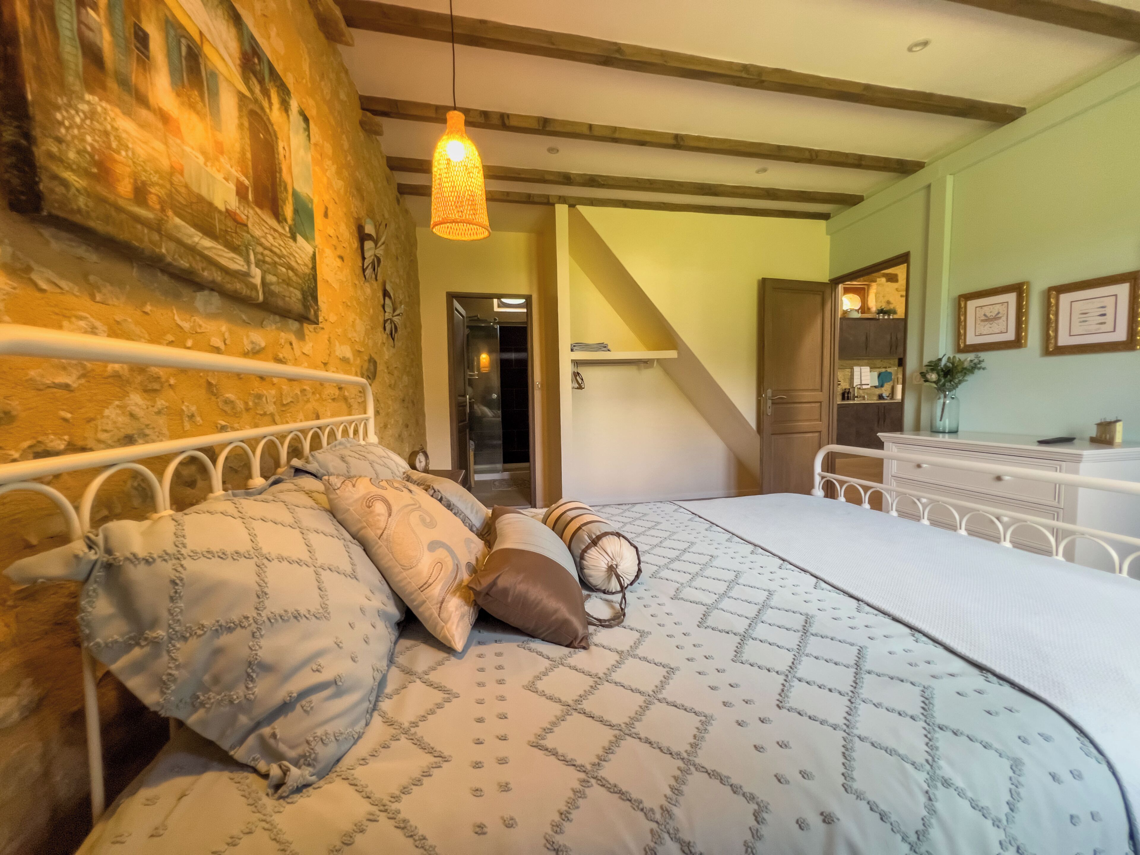 A bedroom with a large bed, a wooden headboard, a hanging light fixture, and a staircase leading to an upper level.