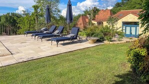 Eine Terrasse mit Liegestühlen und Sonnenschirmen, ein Garten mit unterschiedlichen Pflanzen und ein Haus mit rotem Dach.