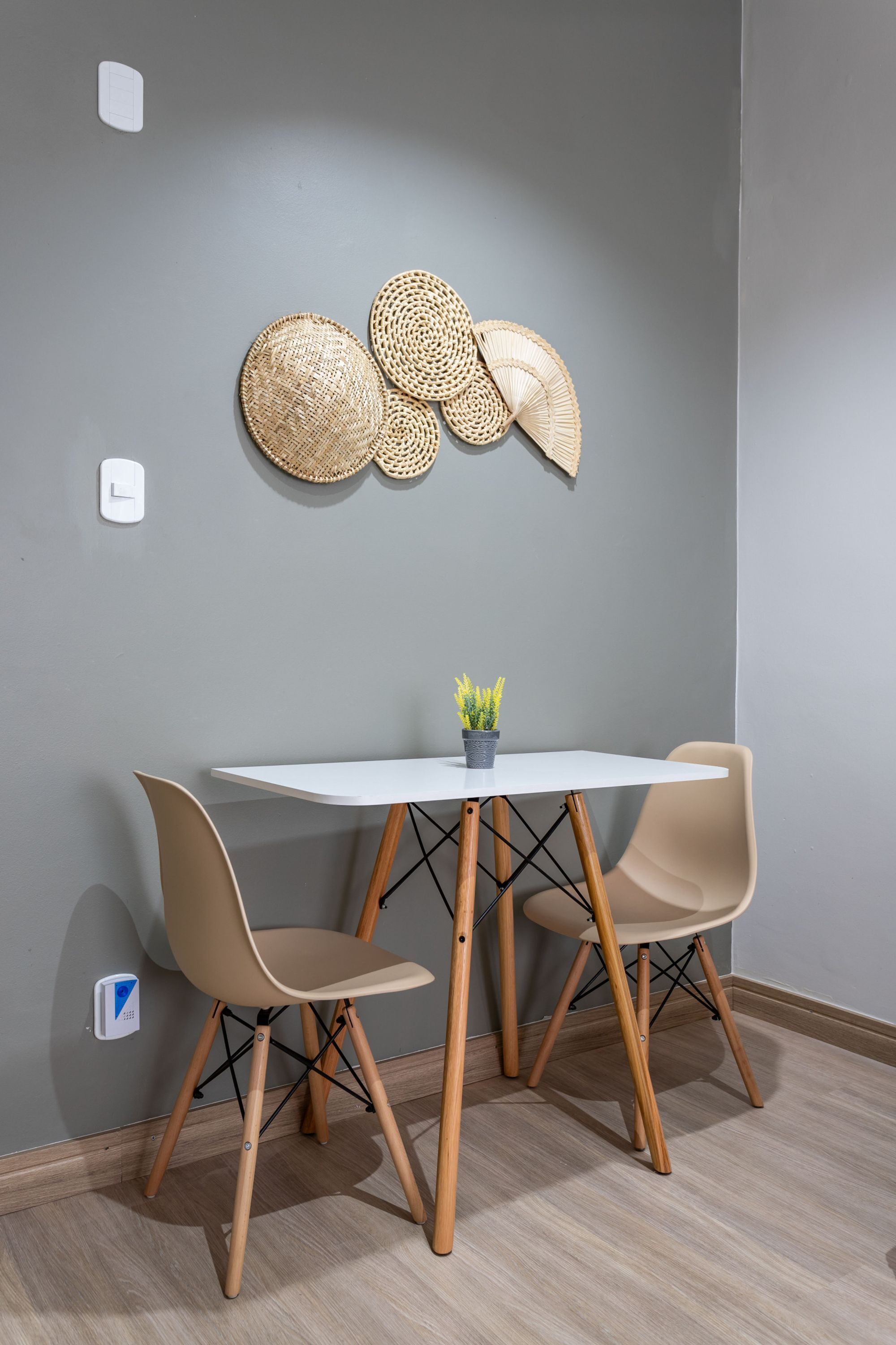 Een eethoek met een witte tafel en twee stoelen, een kleine potplant en geweven wanddecoraties.