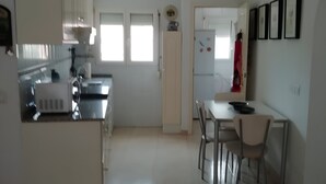 Een ruime keuken met witte kasten, een eethoek met tafel en stoelen, en een koelkast.
