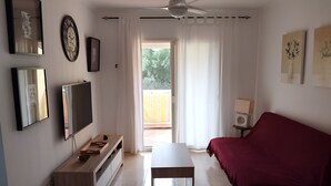 Een moderne woonkamer met een flatscreen televisie, een houten entertainmentkast, een rode bank, een kleine tafel en een plafondventilator.