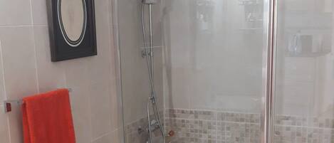 Une salle de bain moderne avec une douche à parois de verre, des toilettes blanches et une serviette rouge posée sur un porte-serviettes.