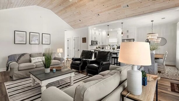 A modern living room with a sofa, armchairs, a coffee table, and a dining area with a chandelier. - Coastal Retreat by Golf & Water; Screened Porch (Townsend)