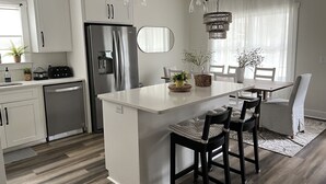 A modern kitchen with white cabinetry, a stainless steel refrigerator, and a central island with chairs. - Coastal Retreat by Golf & Water; Screened Porch (Townsend)