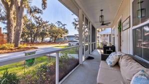 A covered porch with a sofa, a ceiling fan, and a view of a road and trees. - Coastal Retreat by Golf & Water; Screened Porch (Townsend)