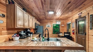 A wooden cabin interior with a kitchen area featuring a large island, wooden cabinets, and a stone countertop. - Stone-Built Cabin w/ Indoor Pool, Firepit, & Bunk Room @ Smokies Retreat! (Sevierville)