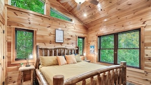 A wooden cabin bedroom with a large bed, two windows, and a ceiling fan. - Log Cabin Retreat in the Smoky Mountain:Private Hot Tub, Billiards, Arcade Games (Gatlinburg)