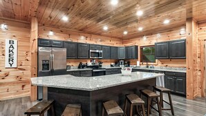 A modern kitchen with wooden walls, granite countertops, and stainless steel appliances. - Log Cabin Retreat in the Smoky Mountain:Private Hot Tub, Billiards, Arcade Games (Gatlinburg)