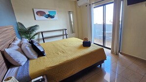 Ein Hotelzimmer mit einem Bett, einem kleinen Tisch, einer Topfpflanze und Blick auf den Außenbalkon.