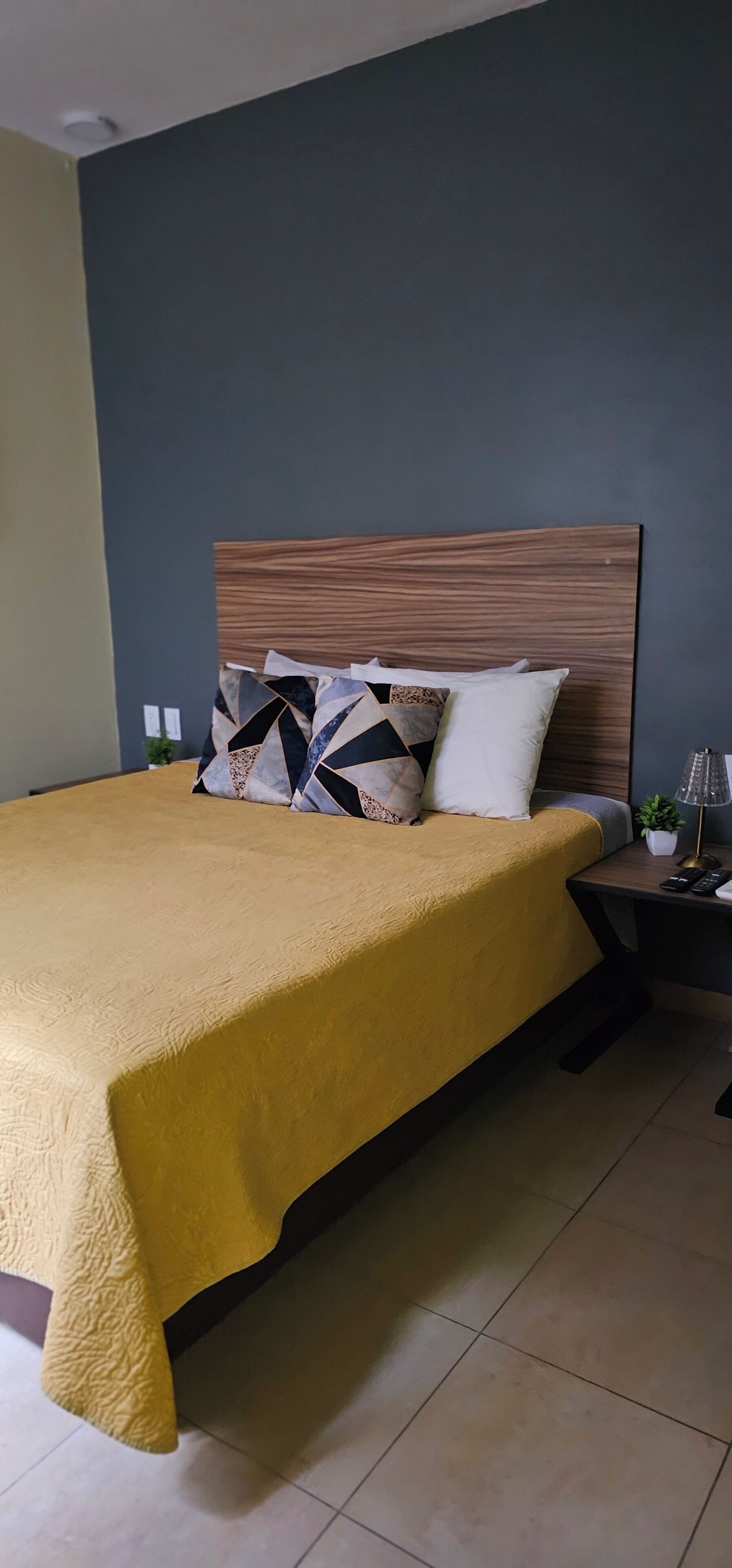 Een bed met een gele sprei, een houten hoofdbord en meerdere kussens.