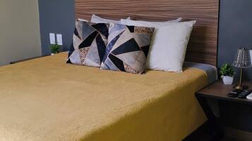 Een bed met een gele sprei, een houten hoofdbord en meerdere kussens.