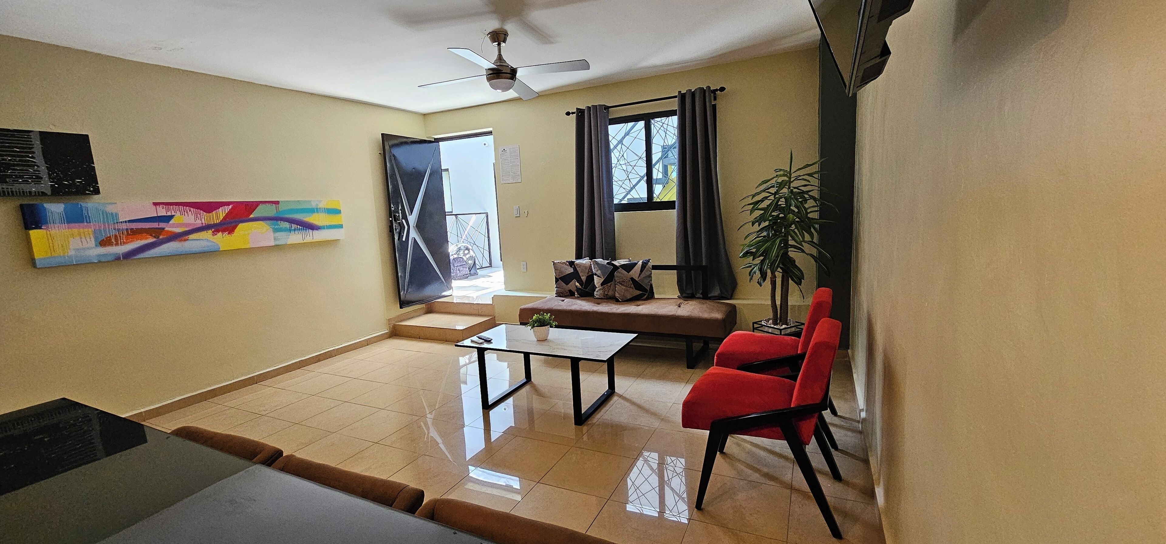 A living room with a sofa, red chairs, a coffee table, and a ceiling fan.