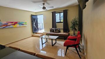 A living room with a sofa, red chairs, a coffee table, and a ceiling fan.