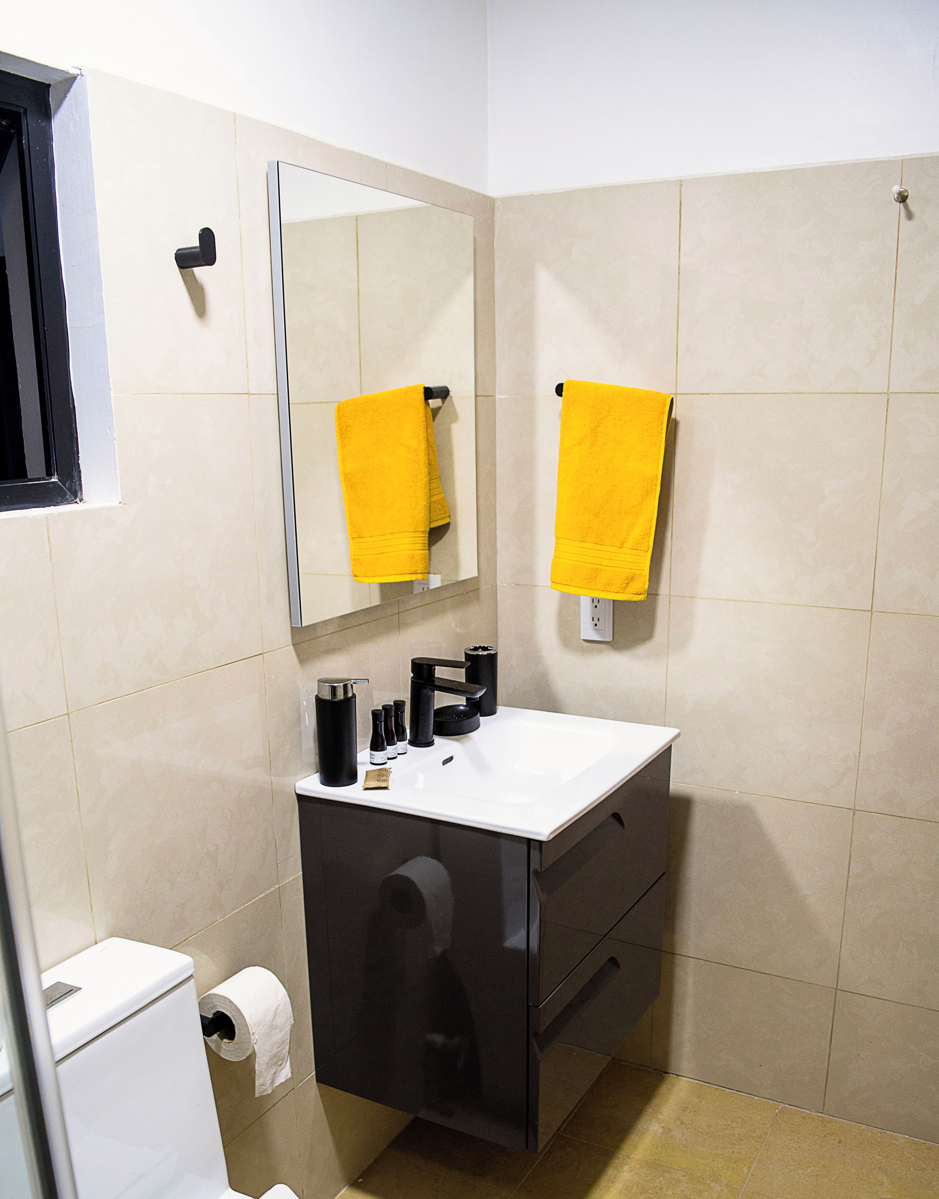 Une salle de bain avec un lavabo blanc, un meuble noir et une serviette jaune accrochée au mur.