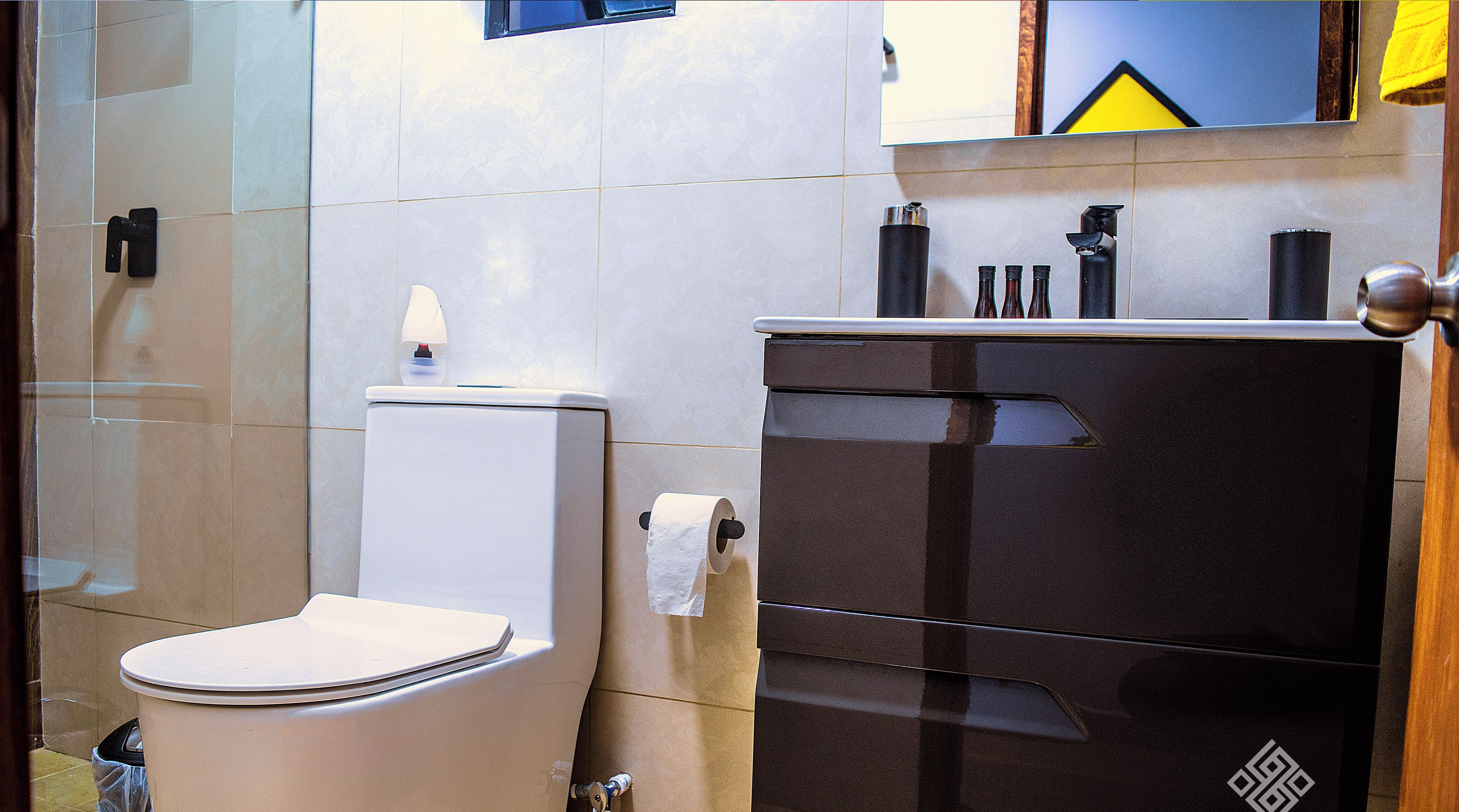 Un baño moderno con inodoro, un cesto de basura y un mueble negro con un logotipo.