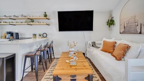A modern living room with a white sofa, a wooden coffee table, and a TV mounted on the wall.