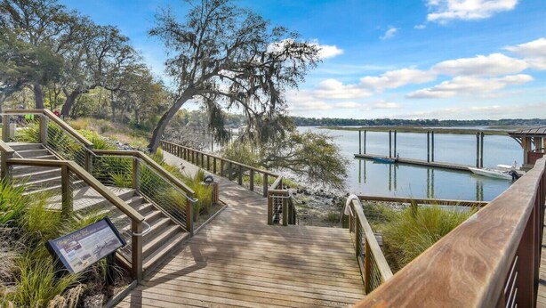 A wooden boardwalk leading to a dock over a calm body of water, surrounded by trees and a clear sky.