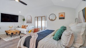A modern bedroom with a bed, a TV, a ceiling fan, and a large window.